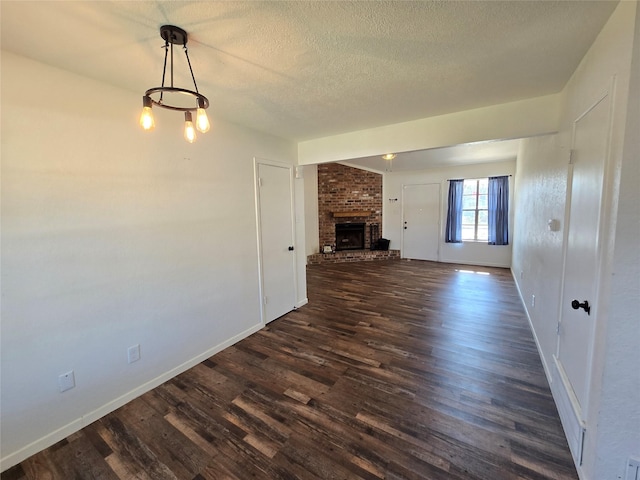 unfurnished living room featuring a fireplace, a chandelier, a textured ceiling, and dark hardwood / wood-style floors