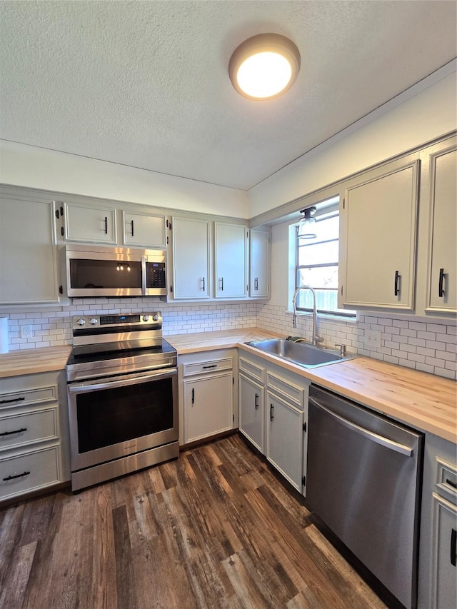 kitchen with stainless steel appliances, dark hardwood / wood-style flooring, butcher block countertops, decorative backsplash, and sink