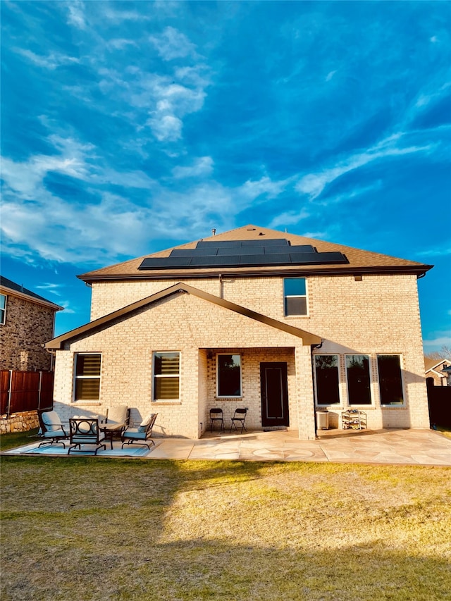 rear view of property featuring a lawn, solar panels, and a patio