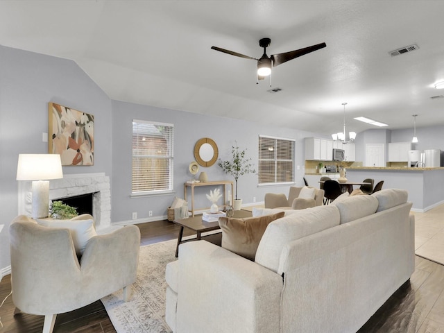 living room featuring ceiling fan with notable chandelier, hardwood / wood-style floors, lofted ceiling, and a stone fireplace