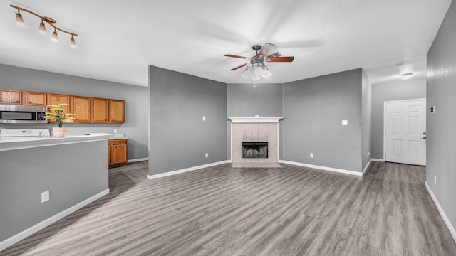 unfurnished living room with light wood-style flooring, a fireplace, a ceiling fan, and baseboards