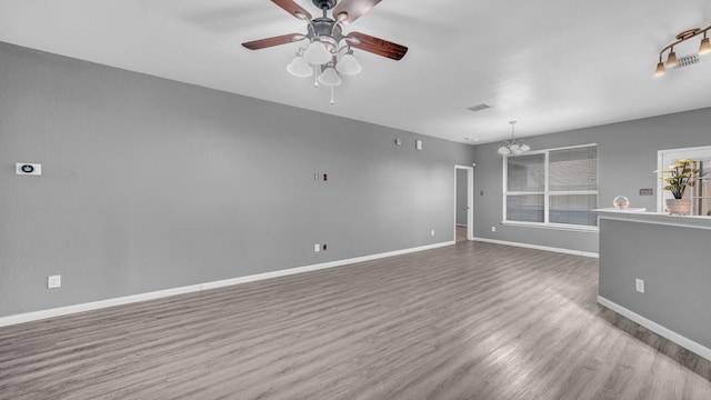 unfurnished living room featuring visible vents, ceiling fan with notable chandelier, baseboards, and wood finished floors