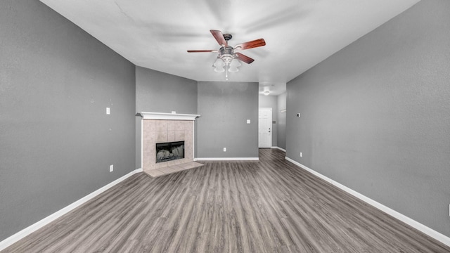 unfurnished living room with baseboards, a ceiling fan, wood finished floors, and a tiled fireplace