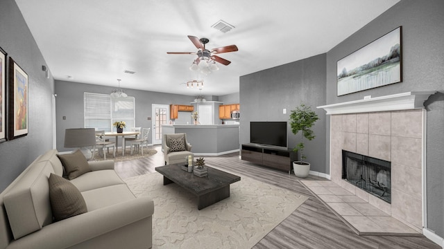 living room featuring light wood finished floors, visible vents, a tile fireplace, and a ceiling fan