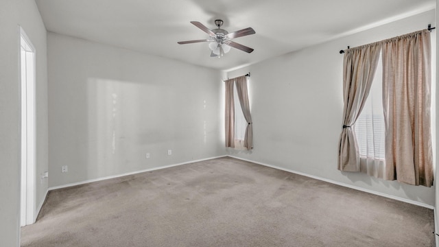 carpeted spare room featuring baseboards and a ceiling fan