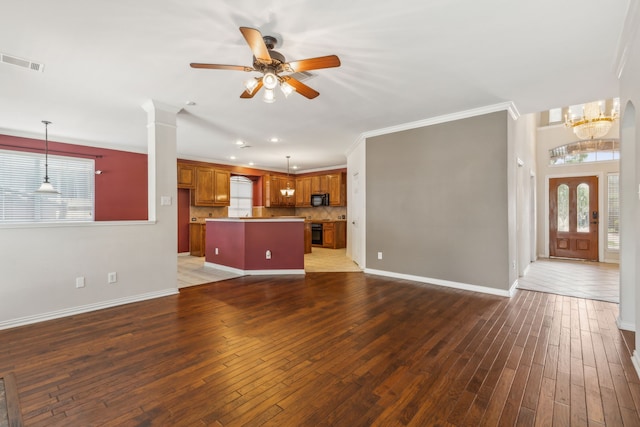 unfurnished living room featuring ceiling fan with notable chandelier, dark hardwood / wood-style floors, plenty of natural light, and crown molding