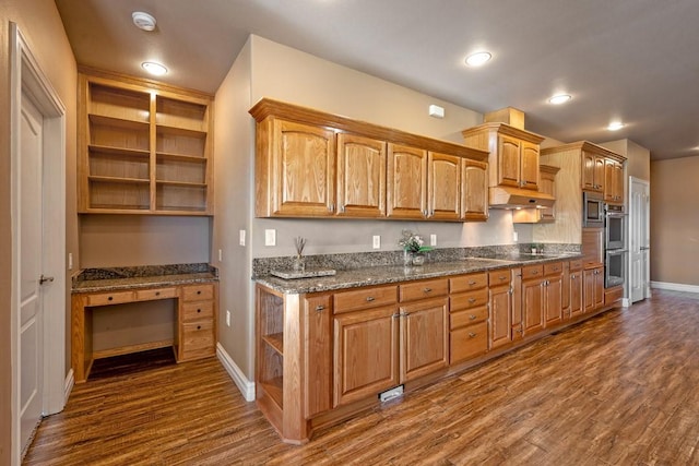 kitchen featuring stainless steel microwave, built in desk, dark wood-type flooring, and dark stone counters