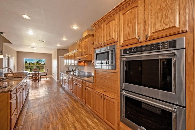 kitchen with appliances with stainless steel finishes, sink, hardwood / wood-style floors, and dark stone counters