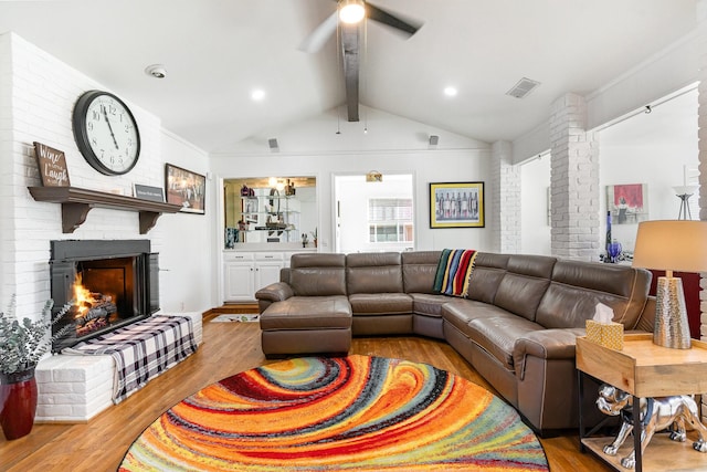 living area with visible vents, a ceiling fan, wood finished floors, vaulted ceiling with beams, and a brick fireplace