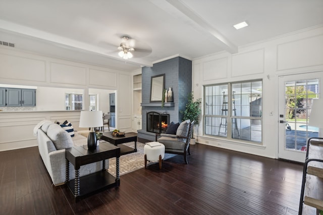 living room with crown molding, a brick fireplace, dark hardwood / wood-style floors, ceiling fan, and beamed ceiling