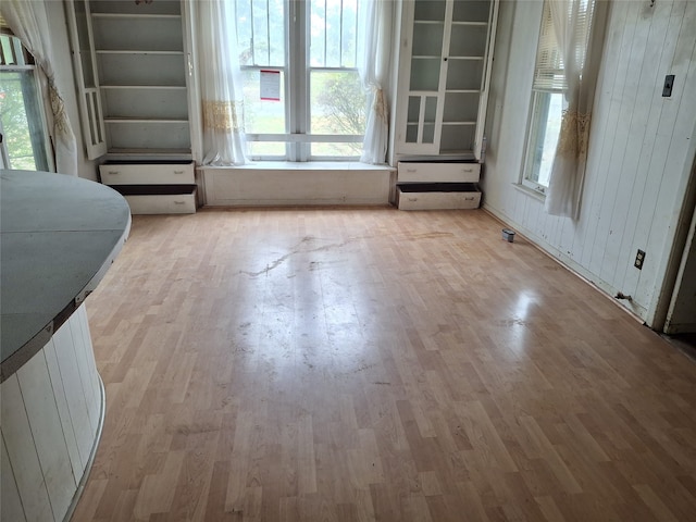 unfurnished dining area with plenty of natural light, wood walls, and light hardwood / wood-style flooring