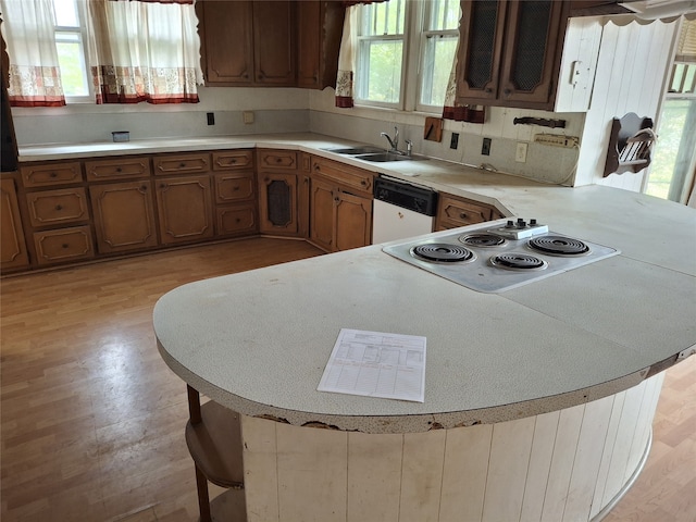 kitchen with kitchen peninsula, a kitchen bar, white appliances, sink, and light hardwood / wood-style flooring