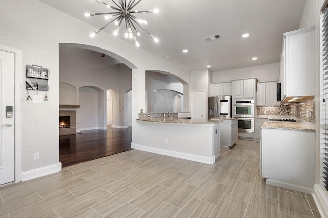 kitchen with light stone countertops, tasteful backsplash, stainless steel appliances, a chandelier, and white cabinetry