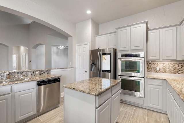 kitchen featuring light stone countertops, tasteful backsplash, stainless steel appliances, a center island, and white cabinetry