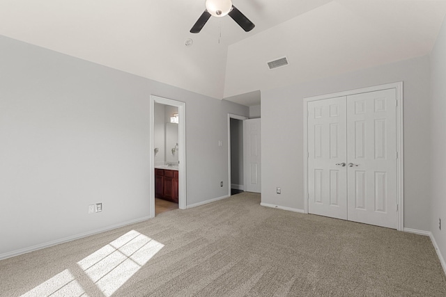 unfurnished bedroom featuring ensuite bath, light colored carpet, vaulted ceiling, ceiling fan, and a closet