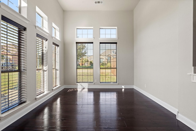 empty room with plenty of natural light, dark hardwood / wood-style floors, and a towering ceiling