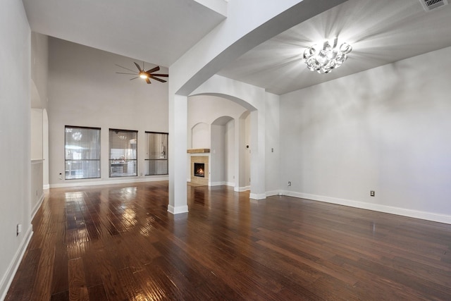 unfurnished living room with ceiling fan, a towering ceiling, and dark wood-type flooring