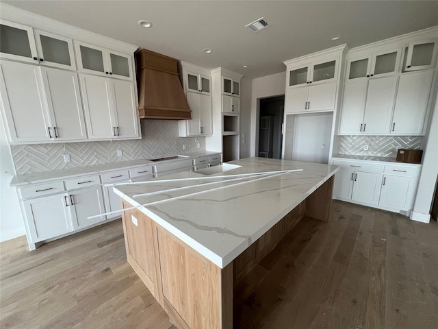 kitchen featuring light wood-type flooring, light stone counters, a spacious island, and custom exhaust hood