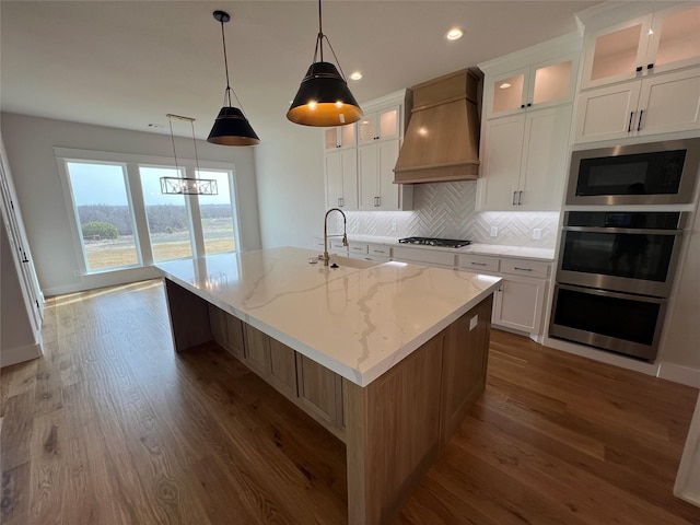 kitchen with premium range hood, a sink, gas stovetop, built in microwave, and a center island with sink