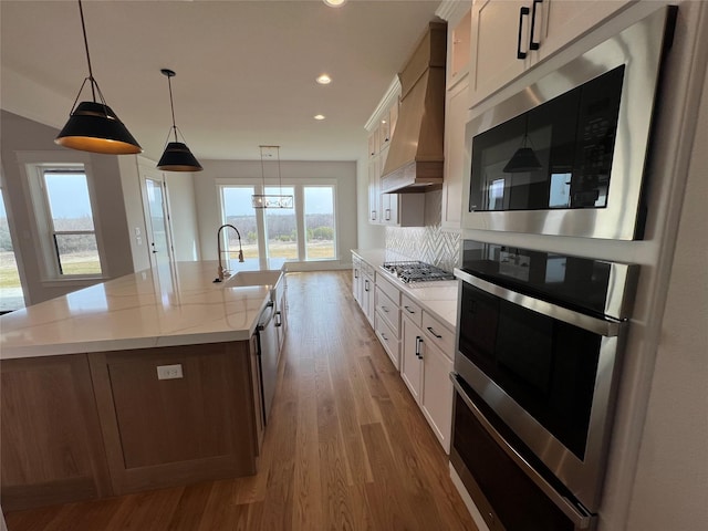 kitchen featuring stainless steel appliances, wood finished floors, a sink, white cabinets, and custom range hood