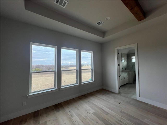 spare room with beamed ceiling, light wood-type flooring, and a healthy amount of sunlight