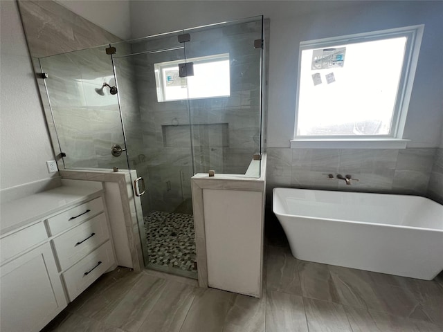 bathroom featuring vanity, independent shower and bath, and tile walls