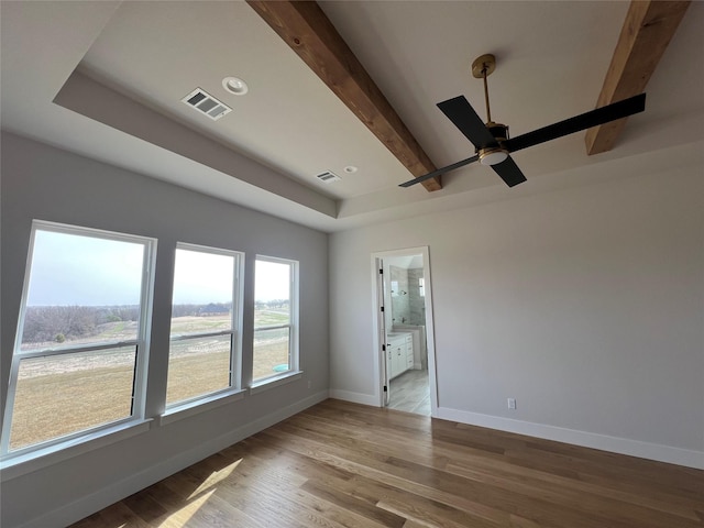 spare room featuring baseboards, visible vents, beamed ceiling, and wood finished floors