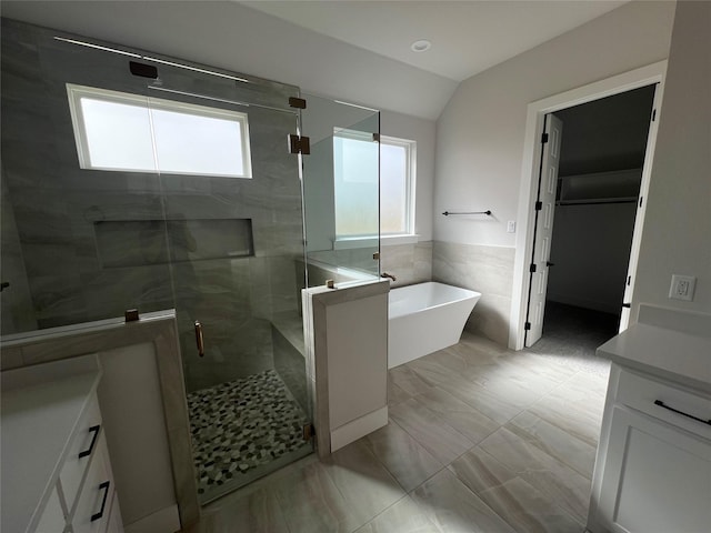 full bath featuring a stall shower, a soaking tub, vaulted ceiling, vanity, and tile walls