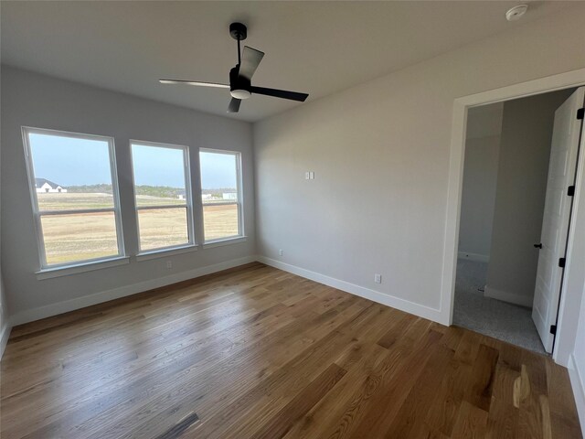 empty room featuring wood finished floors, a ceiling fan, and baseboards