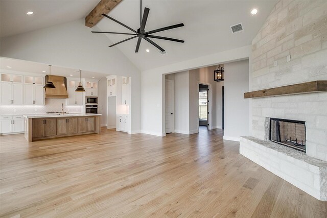 unfurnished living room featuring visible vents, wood finished floors, beamed ceiling, and a stone fireplace