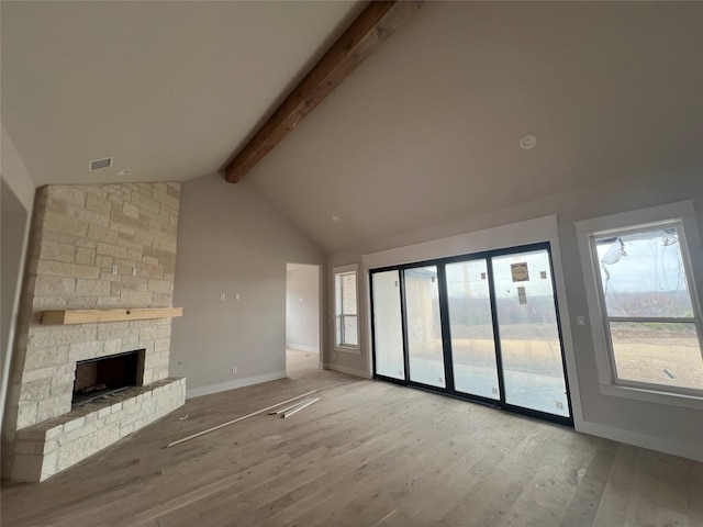 unfurnished living room with beamed ceiling, a healthy amount of sunlight, a stone fireplace, and light hardwood / wood-style flooring