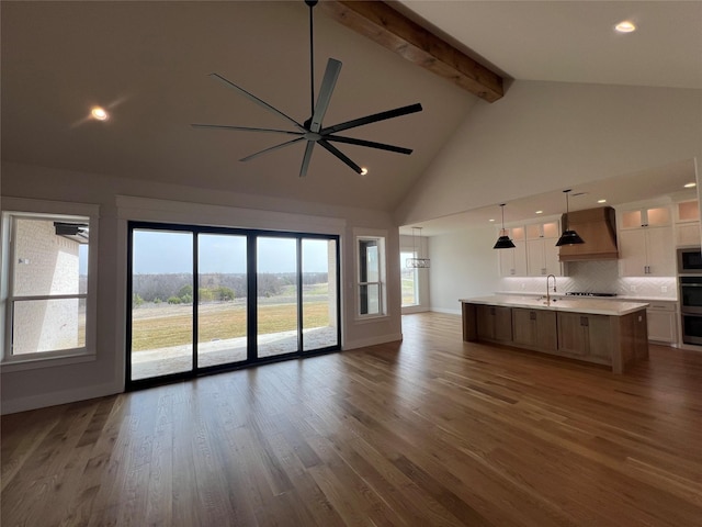 unfurnished living room with beam ceiling, ceiling fan, wood finished floors, high vaulted ceiling, and baseboards