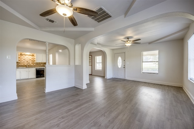 unfurnished living room with wood-type flooring, vaulted ceiling, wine cooler, and ceiling fan