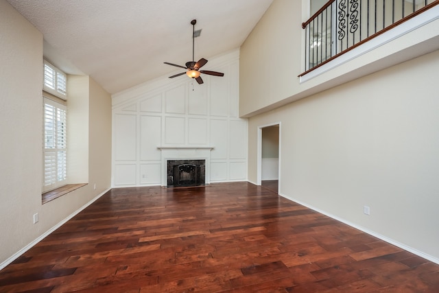 unfurnished living room featuring dark wood-type flooring, a high end fireplace, ceiling fan, a towering ceiling, and a textured ceiling