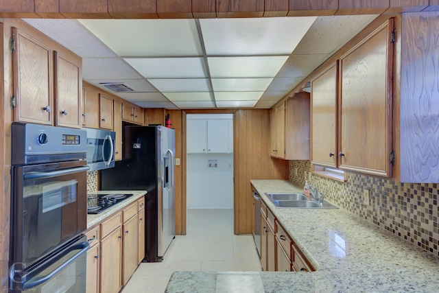 kitchen with sink, a drop ceiling, tasteful backsplash, light tile patterned floors, and black appliances