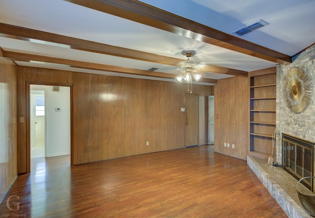 unfurnished living room with a fireplace, hardwood / wood-style floors, wooden walls, and beam ceiling