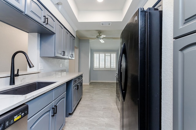 kitchen with black fridge, stainless steel dishwasher, a tray ceiling, ceiling fan, and sink