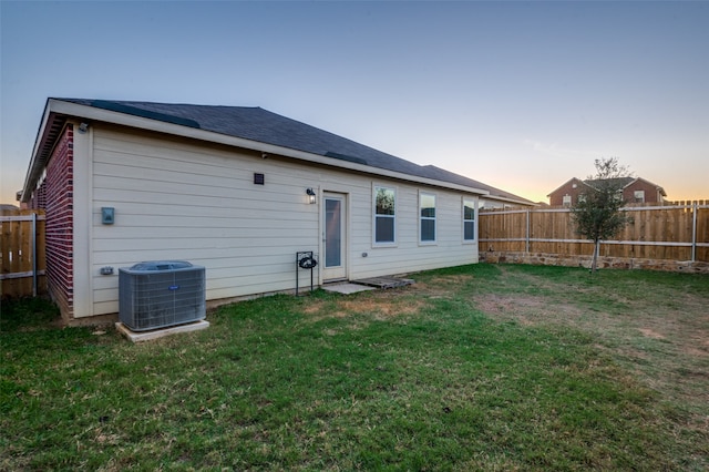 back house at dusk featuring a yard and central air condition unit