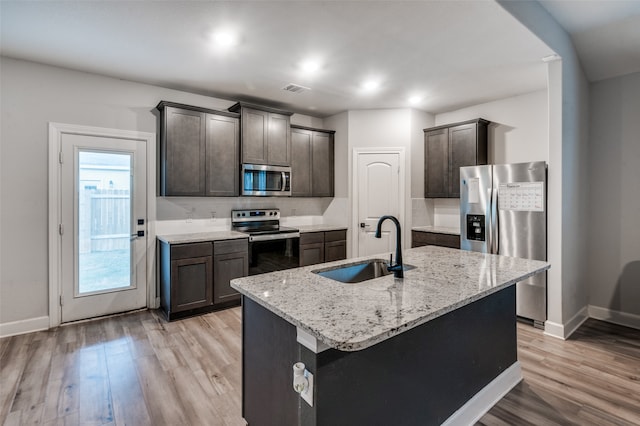 kitchen with appliances with stainless steel finishes, dark brown cabinets, sink, light hardwood / wood-style flooring, and an island with sink