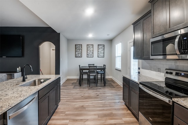 kitchen featuring sink, light hardwood / wood-style flooring, light stone countertops, appliances with stainless steel finishes, and dark brown cabinets