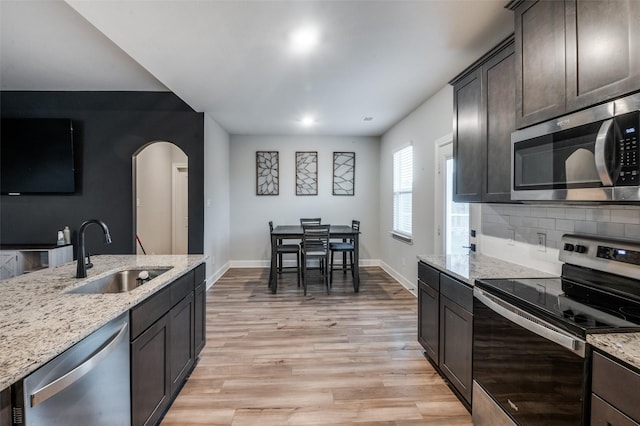 7609 Duck Bay Rd, Fort Worth, TX 76120 - kitchen featuring appliances with stainless steel finishes, a sink, arched walkways, light wood-style flooring, and baseboards