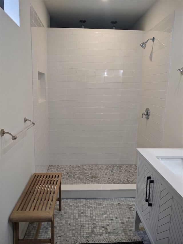 bathroom with tile patterned flooring, a tile shower, and vanity