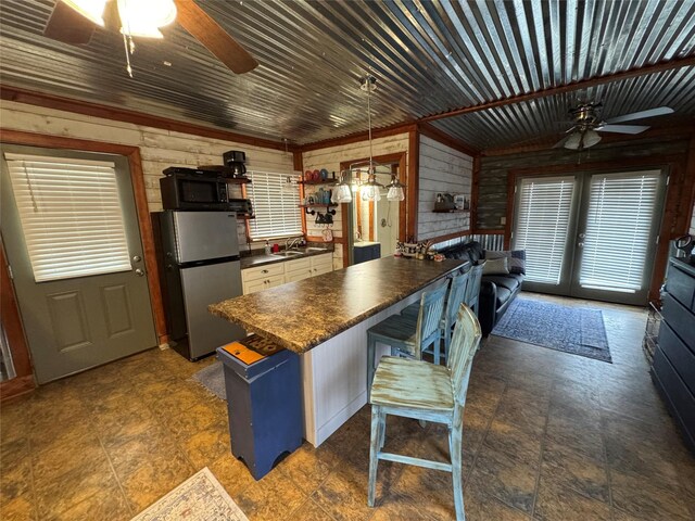 kitchen featuring french doors, a kitchen breakfast bar, hanging light fixtures, wooden walls, and stainless steel refrigerator