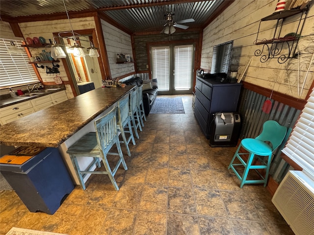 kitchen featuring blue cabinetry, ceiling fan, decorative light fixtures, a kitchen bar, and wooden walls