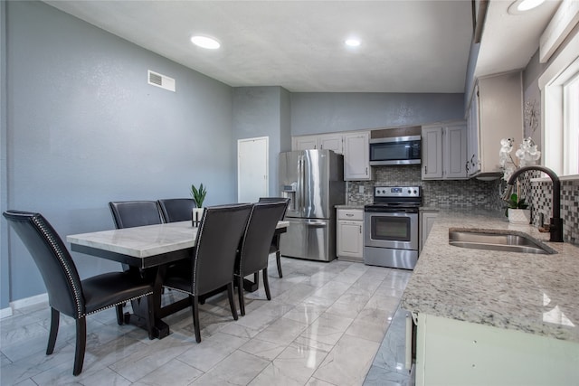 kitchen featuring appliances with stainless steel finishes, tasteful backsplash, light stone counters, vaulted ceiling, and sink