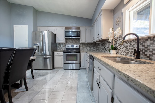 kitchen with lofted ceiling, backsplash, white cabinets, sink, and appliances with stainless steel finishes