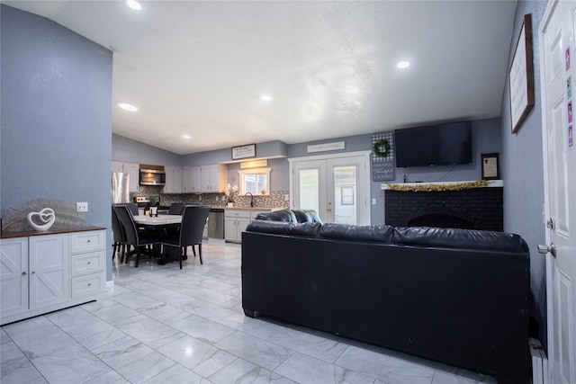 living room with a brick fireplace, french doors, sink, and vaulted ceiling