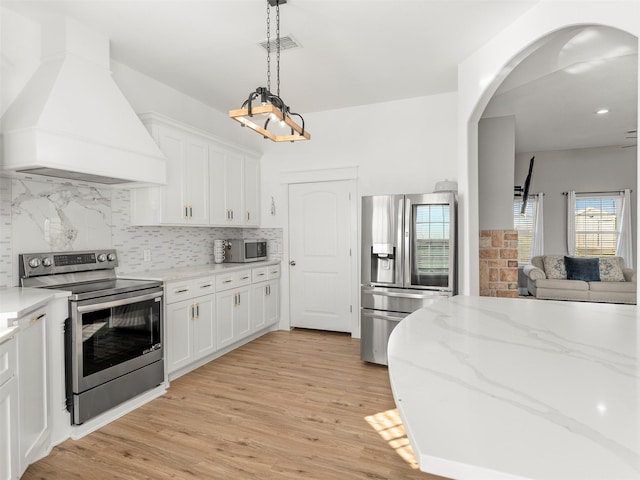 kitchen featuring custom exhaust hood, light wood-type flooring, appliances with stainless steel finishes, light stone counters, and white cabinetry