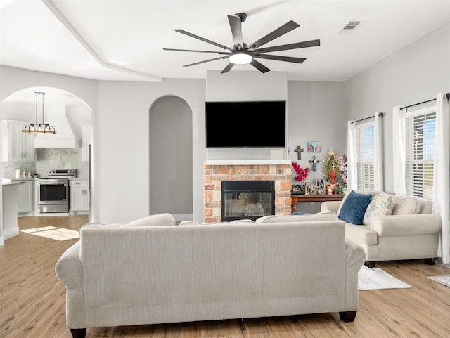 living room featuring light hardwood / wood-style flooring, ceiling fan, and a stone fireplace