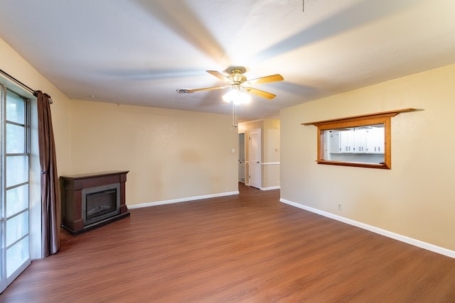 unfurnished living room with a glass covered fireplace, ceiling fan, baseboards, and wood finished floors